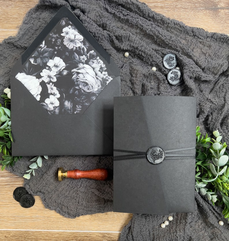 Puede incluir: Invitaci&oacute;n de boda negra con un dise&ntilde;o floral en el sobre interior y un sello de cera negro en el sobre exterior.