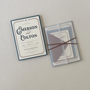 Western wedding invitation paired with translucent layered stationery tied with thin brown ribbon, featuring dusty blue and warm neutral details for an elegant ranch wedding.