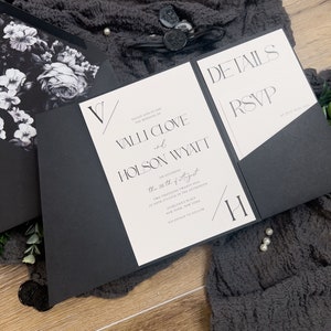Puede incluir: Invitaci&oacute;n de boda en blanco y negro con un dise&ntilde;o floral en el frente y detalles sobre la boda en el interior. La invitaci&oacute;n dice "Por favor, &uacute;nase a nosotros para la boda de Valli Clove y Holson Wyatt el s&aacute;bado 26 de agosto de 2025 a las cuatro de la tarde, Everlynn's Place, Nueva York, Nueva York. Recepci&oacute;n a continuaci&oacute;n."