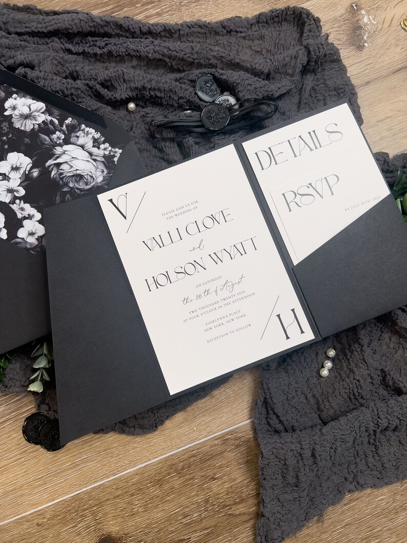 Puede incluir: Invitaci&oacute;n de boda en blanco y negro con un dise&ntilde;o floral en el frente y detalles sobre la boda en el interior. La invitaci&oacute;n dice "Por favor, &uacute;nase a nosotros para la boda de Valli Clove y Holson Wyatt el s&aacute;bado 26 de agosto de 2025 a las cuatro de la tarde, Everlynn's Place, Nueva York, Nueva York. Recepci&oacute;n a continuaci&oacute;n."