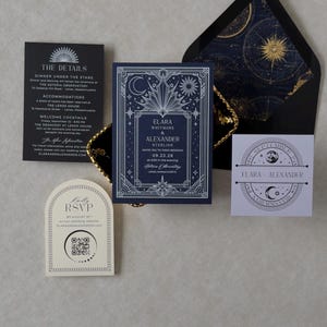 Elara navy blue wedding invitation with ornate silver Art Deco celestial border, displayed alongside a black envelope with gold astronomical liner, black details card, ivory arch RSVP, and lavender celestial tag.