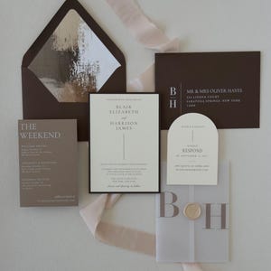Neutral wedding invitation suite featuring an ivory bordered invitation, brown details card, arch RSVP card and translucent vellum monogram overlay in warm taupe and chocolate tones.