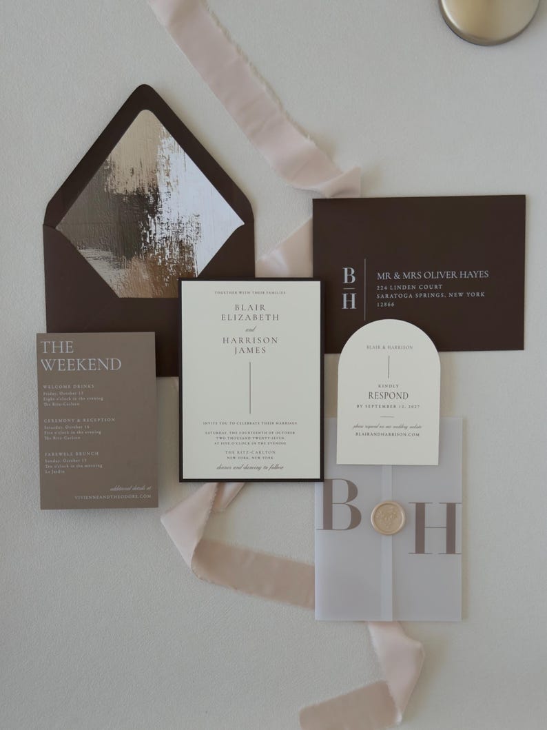 Neutral wedding invitation suite featuring an ivory bordered invitation, brown details card, arch RSVP card and translucent vellum monogram overlay in warm taupe and chocolate tones.