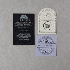 Elara wedding invitation accessories arranged on a neutral textured background, including a black details card with white printing, ivory arch-shaped RSVP card with QR code, and lavender square tag featuring a celestial moon and stars design.