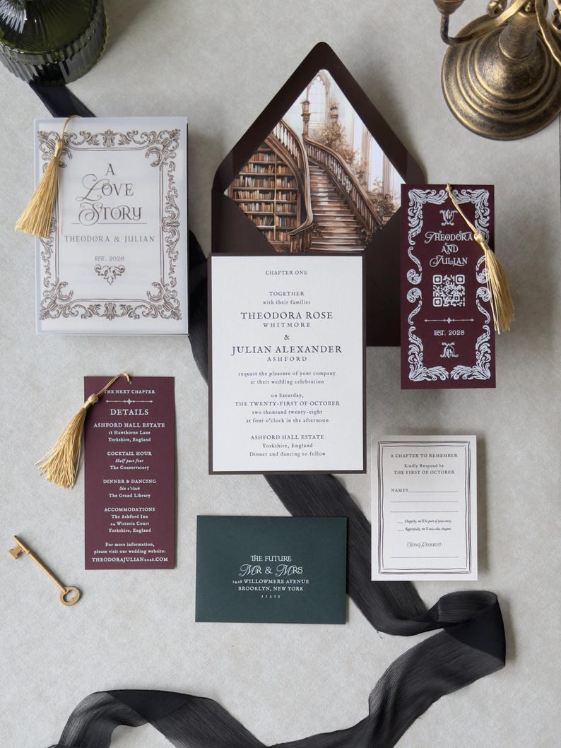 Theodora romantic book-themed wedding invitation suite with ivory invitation, burgundy details card, ornate coordinating inserts, dark brown envelope with grand library staircase liner, and a burgundy bookmark with gold tassel.