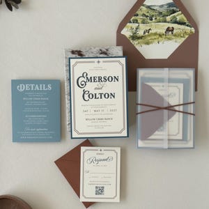 Emerson ranch wedding invitation suite styled with a warm brown envelope, landscape liner, dusty blue details card and translucent layered stationery tied with ribbon.