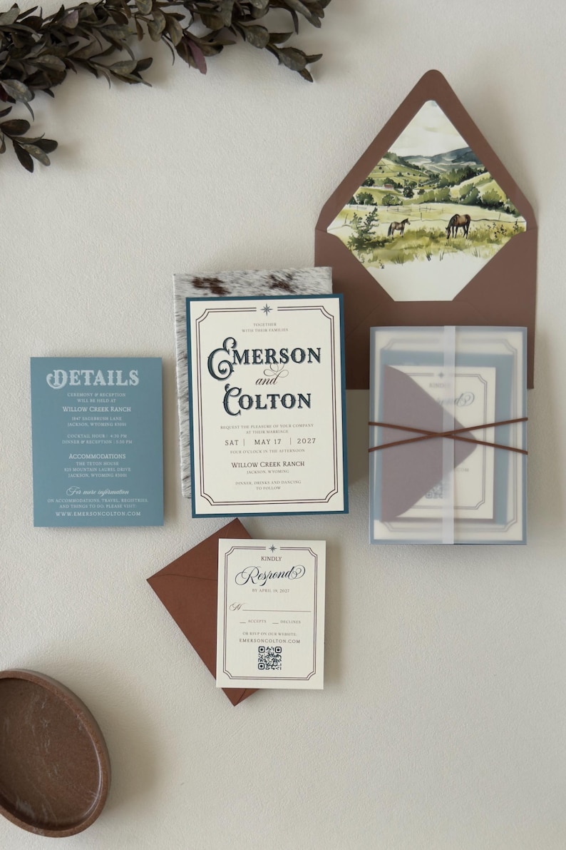 Emerson ranch wedding invitation suite styled with a warm brown envelope, landscape liner, dusty blue details card and translucent layered stationery tied with ribbon.