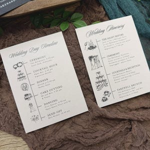 May include: Two wedding itinerary cards with elegant calligraphy. The cards detail the wedding day timeline and the night before events. The cards are on a textured brown fabric with green foliage.
