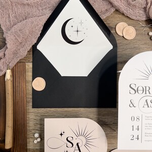 May include: A black and white wedding invitation with a moon and stars design. The invitation is on a pink background with the initials "SA" in a stylized infinity symbol. The text on the invitation reads "SOR & AS" and "KINDLY RSVP BY JULY 16, 2024".