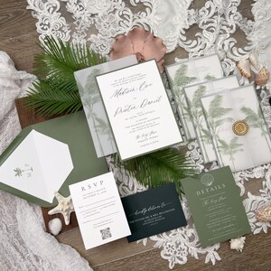 May include: An assortment of wedding stationery featuring a tropical theme. The invitations, RSVP cards, and details cards are in shades of green and white, with palm tree illustrations. The stationery is arranged with seashells and greenery.