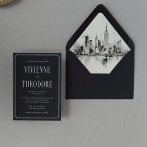 Modern black wedding invitation paired with a black envelope opened to reveal a detailed monochrome city skyline liner for an elegant urban wedding.