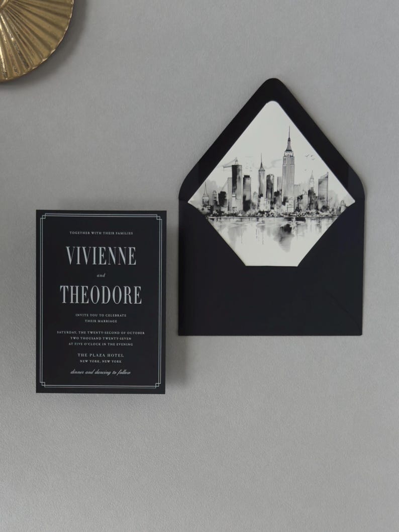 Modern black wedding invitation paired with a black envelope opened to reveal a detailed monochrome city skyline liner for an elegant urban wedding.