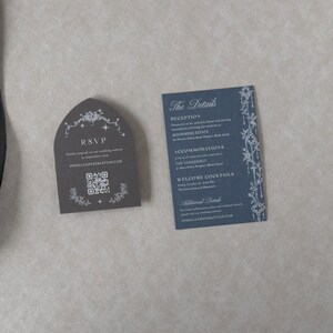 Marina blue wedding details card with white ink typography beside a Dark Grey tombstone-shaped RSVP card featuring decorative celestial artwork and a QR code for online wedding responses.