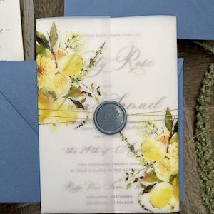 May include: A translucent vellum wedding invitation wrap featuring a watercolor lemon and foliage print, secured with a blue wax seal and gold metallic thread. The invitation text is visible through the vellum, paired with a blue envelope.