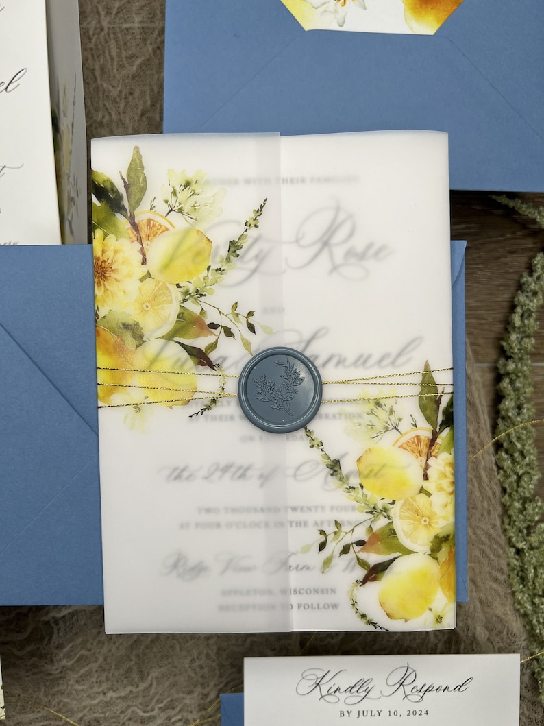 May include: A translucent vellum wedding invitation wrap featuring a watercolor lemon and foliage print, secured with a blue wax seal and gold metallic thread. The invitation text is visible through the vellum, paired with a blue envelope.