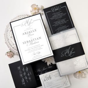 Puede incluir: Un conjunto de invitaciones de boda con tarjetas en blanco y negro con tipograf&iacute;a elegante. El set incluye una invitaci&oacute;n principal, una tarjeta de detalles, una tarjeta RSVP y un sobre negro, decorados con una faja monogramada.