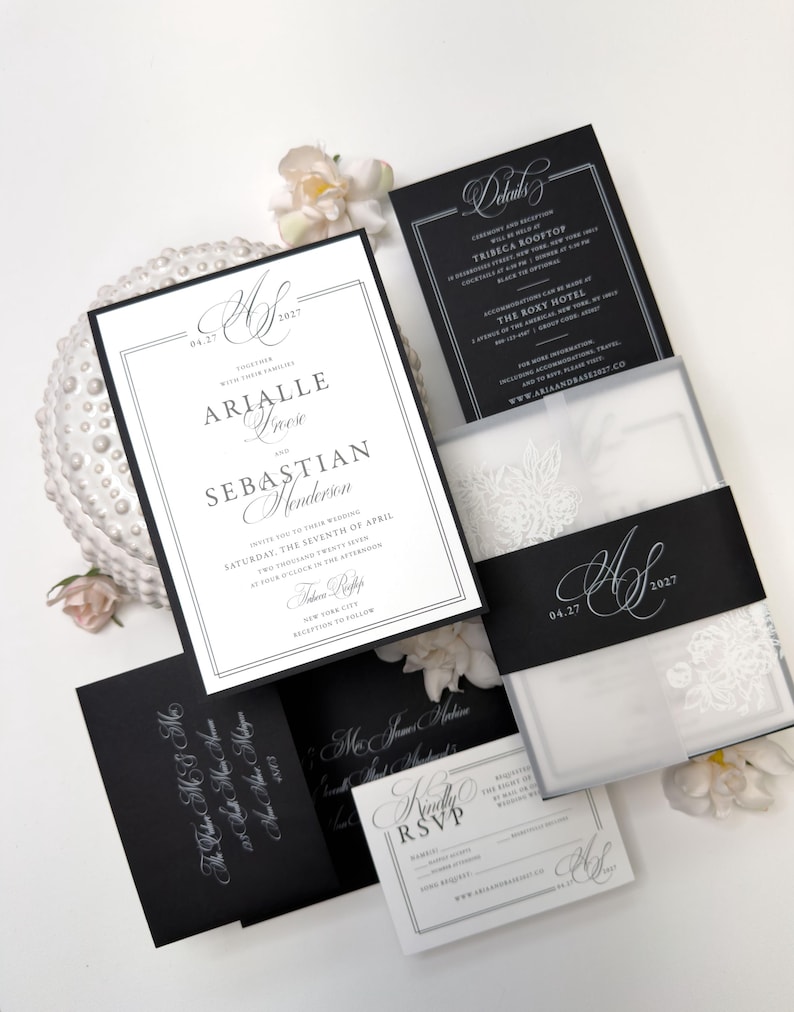 Puede incluir: Un conjunto de invitaciones de boda con tarjetas en blanco y negro con tipograf&iacute;a elegante. El set incluye una invitaci&oacute;n principal, una tarjeta de detalles, una tarjeta RSVP y un sobre negro, decorados con una faja monogramada.
