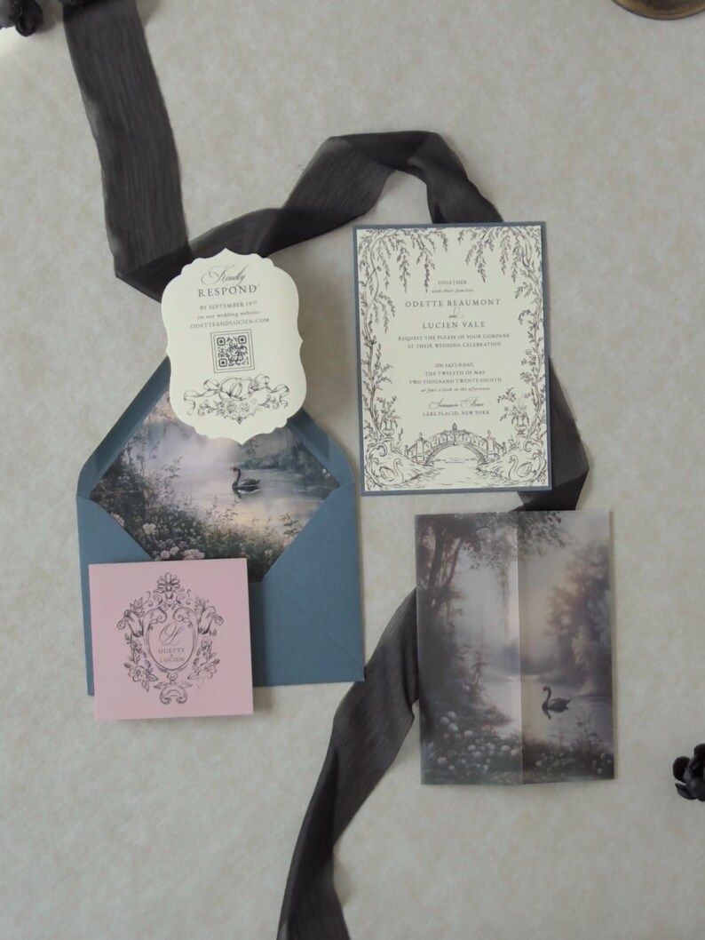 Odette storybook wedding invitation featuring delicate botanical artwork on Cloud Ivory cardstock, layered over Marina blue backing with coordinating scalloped RSVP, illustrated lake vellum jacket, and elegant dark ribbon.