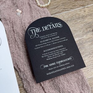 May include: Black and white wedding invitation with a decorative arch design. The invitation details the ceremony and reception location, time, and contact information for accommodations. The text reads "The Details", "Elizabeth Manor", "223 Eastern Ridge Street, New Orleans, Louisiana", "Cocktail Hour at 5:00 pm | Dinner served at 6:00 pm", "Accommodations", "A block of rooms has been reserved at The Hilton Garden Inn with a special rate", "Please call 800.233.1234", "Wedding Group Code: V12024", "For More Information", "Please visit our wedding website: SORAYAANDASPEN.2024.CO".