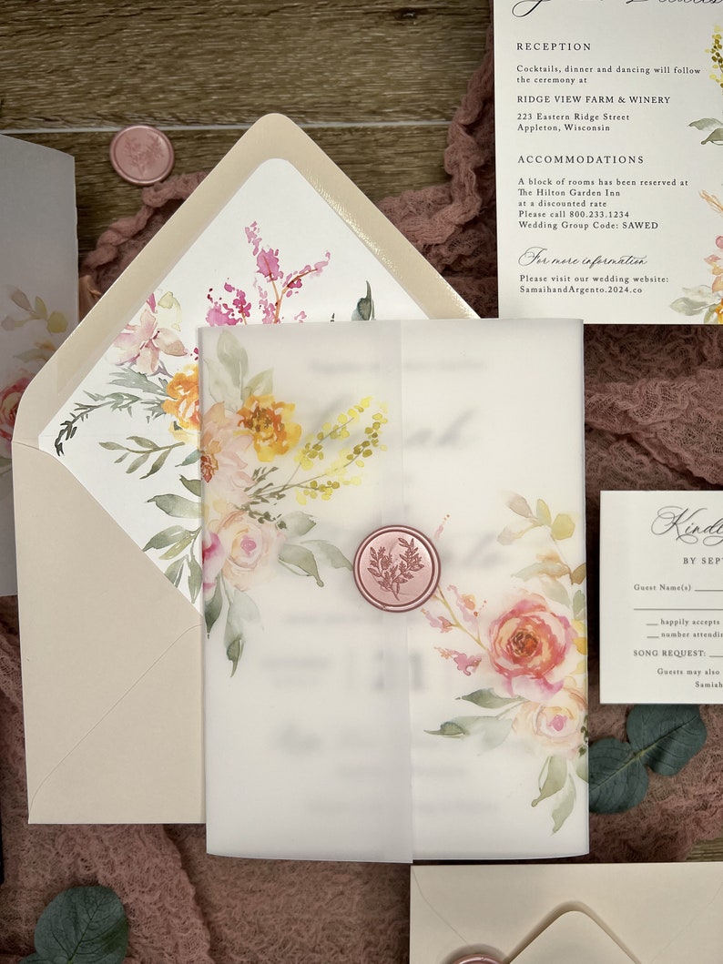 May include: A wedding invitation suite featuring a translucent vellum wrap secured with a pink wax seal, decorated with watercolor floral illustrations in shades of pink, yellow, and green, accompanied by a matching envelope and information card.