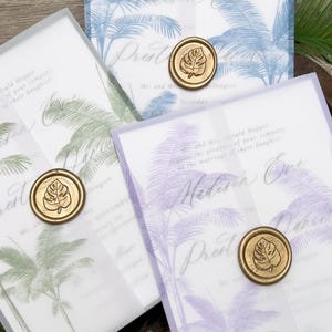 May include: Wedding invitations with a tropical palm tree design in blue, green, and purple. Each invitation is sealed with a gold wax stamp featuring a leaf. The invitations are layered with translucent vellum.