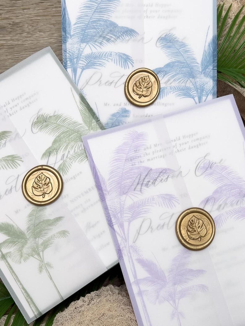 May include: Wedding invitations with a tropical palm tree design in blue, green, and purple. Each invitation is sealed with a gold wax stamp featuring a leaf. The invitations are layered with translucent vellum.
