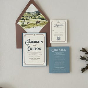 Warm brown envelope with scenic ranch landscape liner displayed with the ivory Emerson invitation, dusty blue details card and square RSVP card.