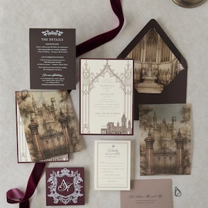 May include: A wedding invitation suite featuring a cream-colored main card with gothic arch illustrations, a dark brown details card, a response card, and envelopes. The set includes vellum overlays with gate imagery and a burgundy monogram card.