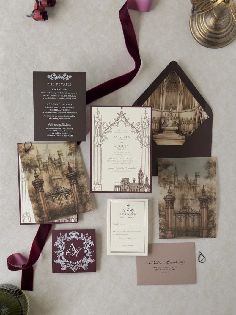 Aurelia Gothic castle wedding invitation suite featuring a Wedding Cream invitation with Bitter Chocolate backing, printed castle-gate vellum overlay, dark brown details card, ivory RSVP, Cashmere RSVP envelope, and Claret decorative crest tag. Styled with burgundy velvet ribbon and Gothic architectural envelope liner.