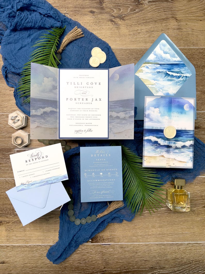 May include: Wedding invitation suite with a beach theme. The invitation features a watercolor painting of the ocean and sky. The suite includes an invitation, RSVP card, details card, and envelope. The color scheme is blue and white, with gold accents.