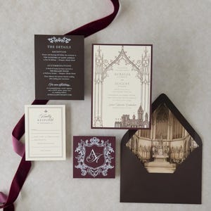 Aurelia Gothic castle wedding invitation flat lay showing architectural vellum overlay, cream invitation, Bitter Chocolate details card and envelope, Cashmere RSVP envelope, and ornate Claret tag on a light textured background.