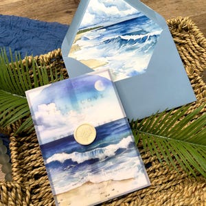 May include: A light blue envelope and invitation featuring a watercolor painting of ocean waves and a sandy beach. The invitation is sealed with a gold wax seal. The text "Tall Cove" is visible on the invitation.