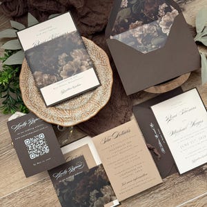 May include: A wedding invitation suite featuring dark brown envelopes with floral liners, cream-colored cards with black serif text, and a response card with a QR code. The set includes a details card and an invitation for Romi Thomas and Michael Hayes.