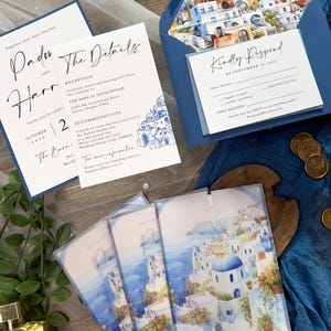 May include: Wedding invitation suite with a blue and white color scheme. The invitation features a watercolor illustration of a Greek island town. The RSVP card has a blue background with white text. The text on the invitation reads "Padi and Harr" and "The Details".