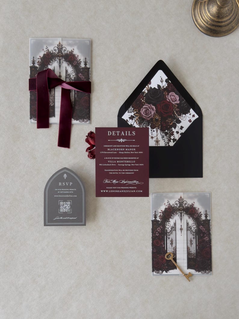 Dark romantic wedding invitation suite featuring a white invitation, Claret details card, printed vellum jacket with black and burgundy roses, Ebony envelope with floral liner, and Dark Grey online RSVP card.