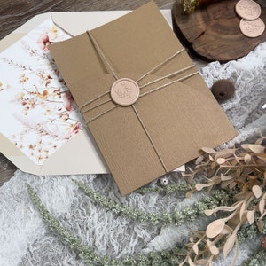 May include: A brown envelope with a white floral design on the front. The envelope is tied with twine and sealed with a pink wax seal. The wax seal has a floral design.