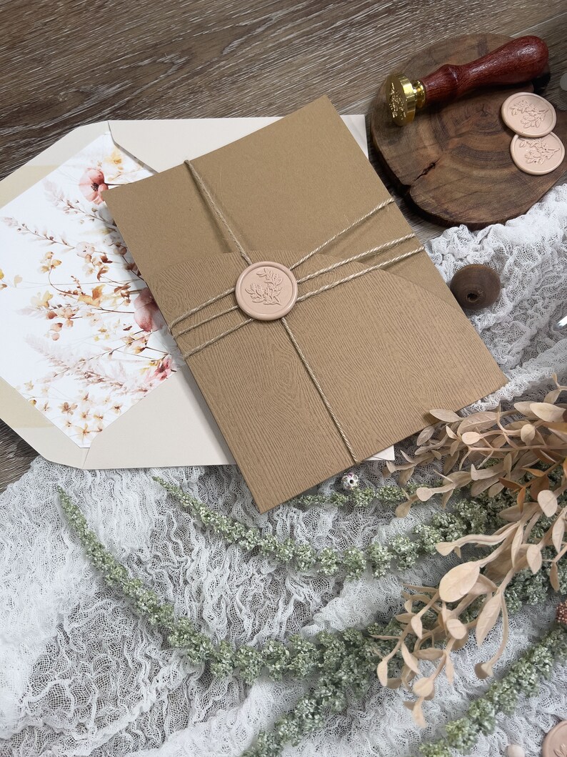 May include: A brown envelope with a white floral design on the front. The envelope is tied with twine and sealed with a pink wax seal. The wax seal has a floral design.