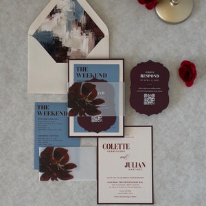 Burgundy and blue floral wedding invitation suite with ivory invitation, dusty blue wedding details card, burgundy scalloped RSVP card and coordinating floral-lined envelope, styled with deep red floral accents.