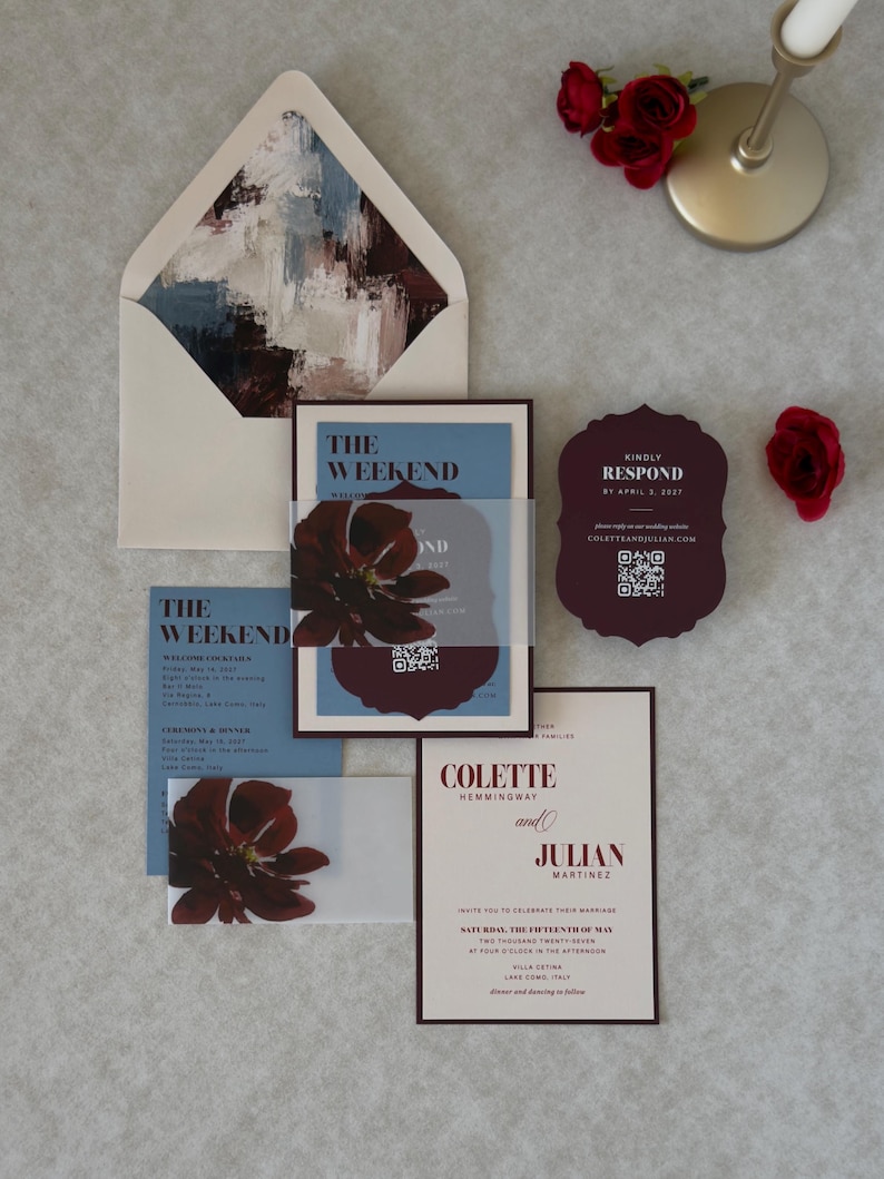 Burgundy and blue floral wedding invitation suite with ivory invitation, dusty blue wedding details card, burgundy scalloped RSVP card and coordinating floral-lined envelope, styled with deep red floral accents.