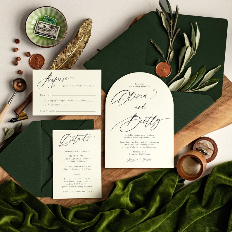 May include: Wedding invitation suite with a green envelope, a white RSVP card, and a white card with a calligraphy design that says "Olivia and Bentley" with details about the wedding ceremony and reception. The text on the card reads "Together with their families, Olivia and Bentley, joyfully invite you to share in their wedding celebration, Saturday, the Eleventh of November, at one o'clock in the afternoon, Marren Hall, 101 South Main Avenue, Oakdale, California, Reception to Follow."
