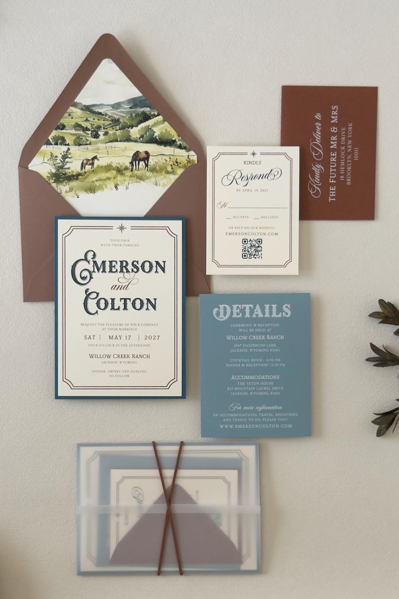 Warm brown envelope with scenic ranch landscape liner displayed with the ivory Emerson invitation, dusty blue details card and square RSVP card.