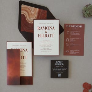 Modern rust and chocolate wedding invitation featuring a warm ivory invitation layered over a dark brown backing mat with a bold abstract envelope liner in earthy terracotta tones.