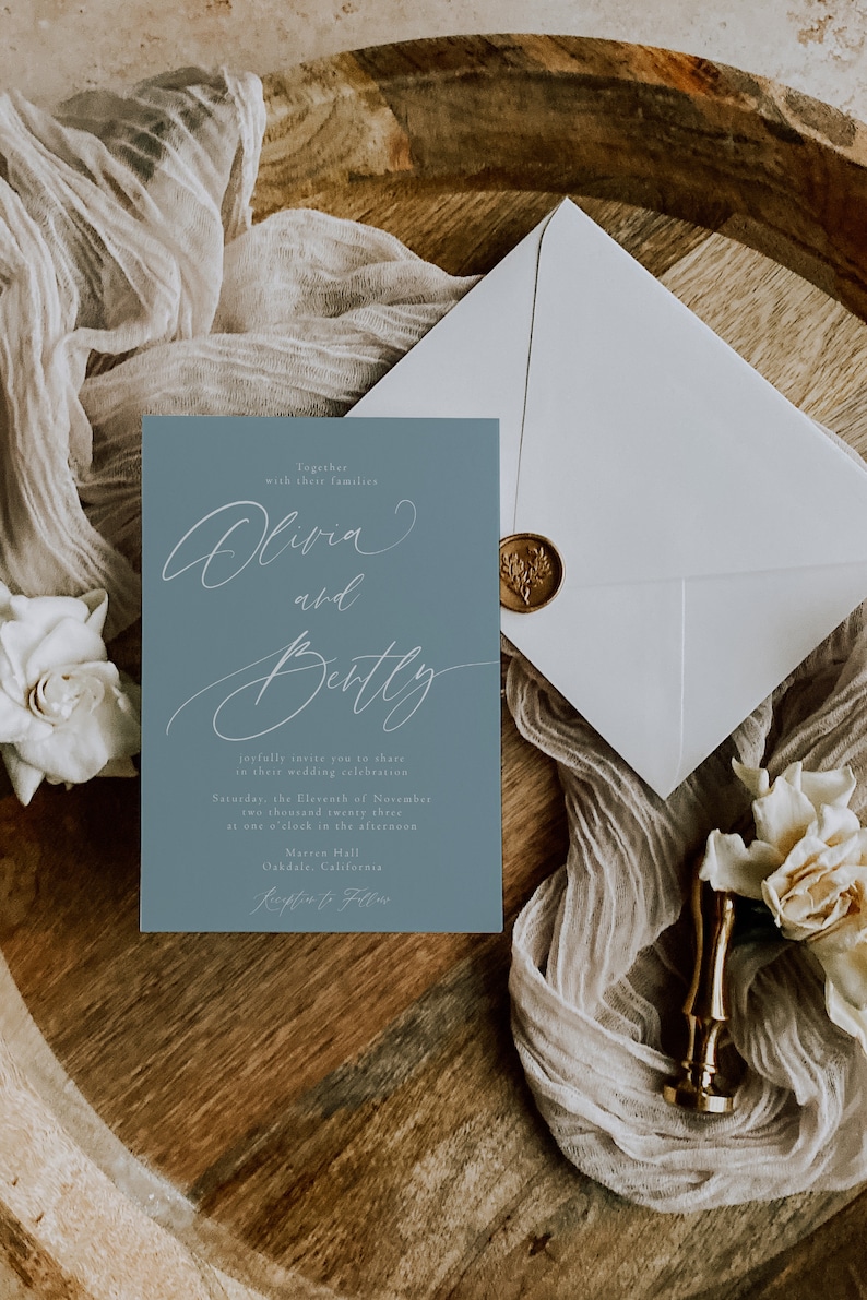 May include: A wedding invitation suite featuring a dusty blue invitation card with elegant script, an envelope with a gold wax seal, and decorative elements. The invitation reads "Olivia and Bentley" and includes event details.