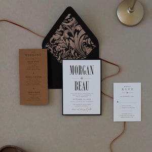 Warm brown wedding details card, white invitation and RSVP card displayed with a black envelope and dramatic botanical liner from the Whitmore wedding suite.