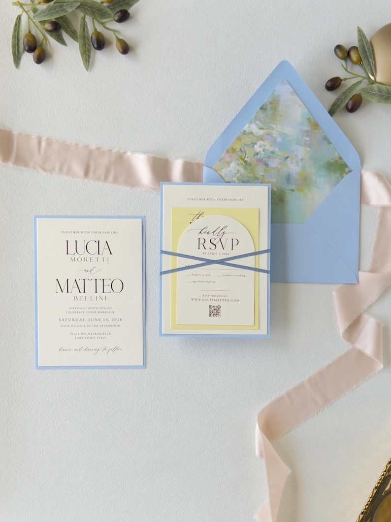 Pale blue wedding envelope opened to reveal a soft watercolor floral liner, paired with the Lucia layered invitation and ivory arched RSVP card.