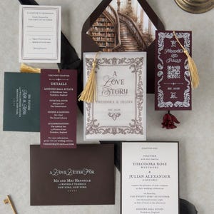 Theodora dark academia wedding invitation suite featuring an ivory invitation with ornate vintage borders, burgundy details card, dark brown envelope, library staircase envelope liner, and burgundy bookmark with gold tassel, arranged in a romantic literary-inspired flat lay.