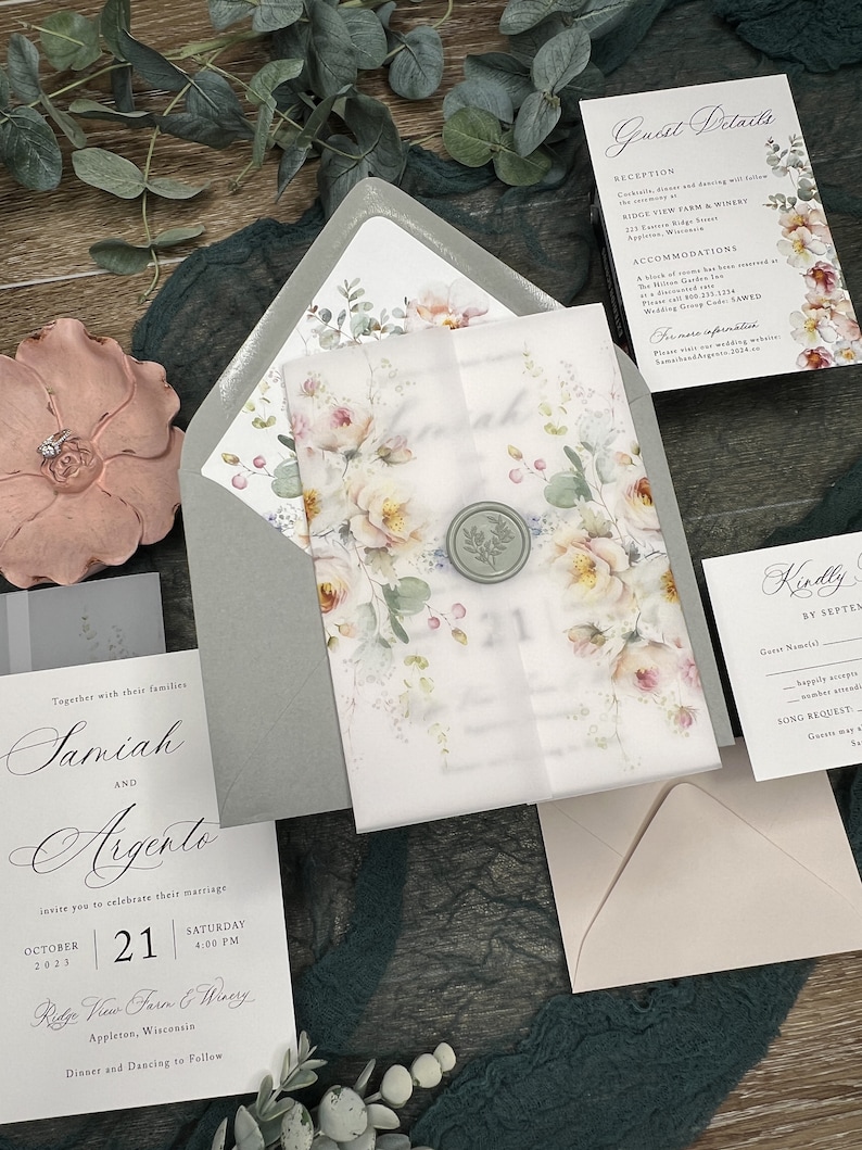 May include: A wedding invitation suite featuring a vellum wrap with a floral print and a sage green wax seal, a grey envelope, a guest details card, a response card, and a main invitation card with black text on white paper, all displaying floral motifs.