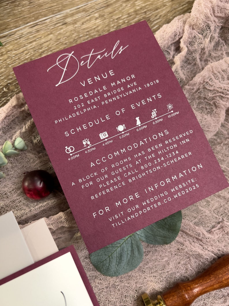 Close-up of burgundy floral wedding invitation with soft pink flowers and romantic botanical styling.