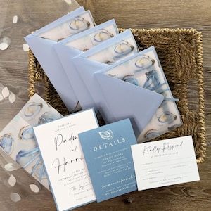 May include: Wedding stationery set featuring oyster illustrations and light blue envelopes. The set includes invitation cards, details cards, and RSVP cards, all presented in a woven basket.