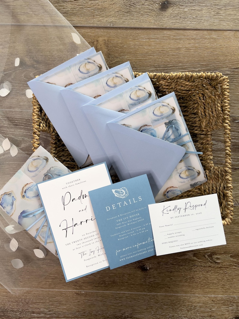 May include: Wedding stationery set featuring oyster illustrations and light blue envelopes. The set includes invitation cards, details cards, and RSVP cards, all presented in a woven basket.